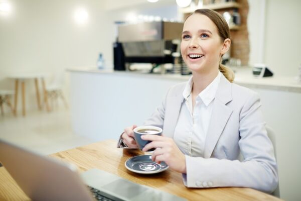 Wanita minum kopi depan laptop di kafe